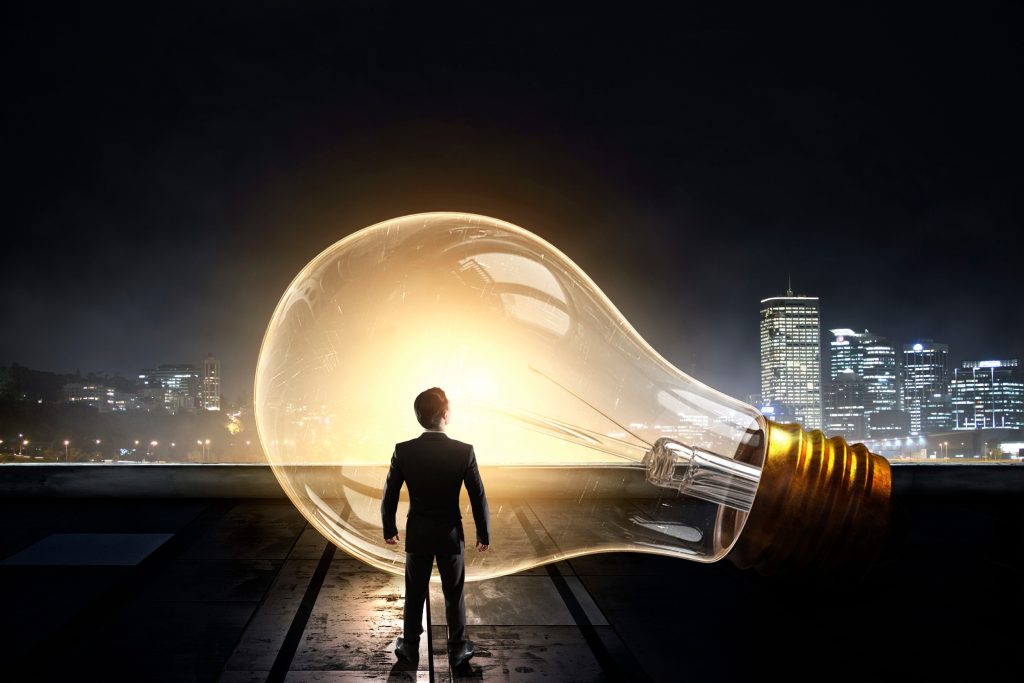 Silhouette of person standing inside glowing lightbulb with city skyline, representing innovative servant leadership vision