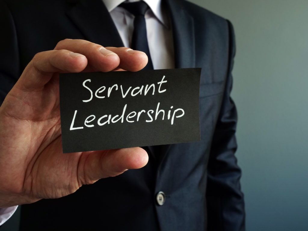 Professional in business suit holding a small chalkboard inscribed with "Servant Leadership