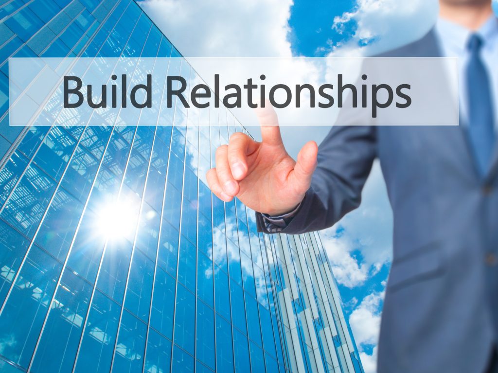 Businessman reaching toward glass building with "Build Relationships" text overlay, representing servant leadership
