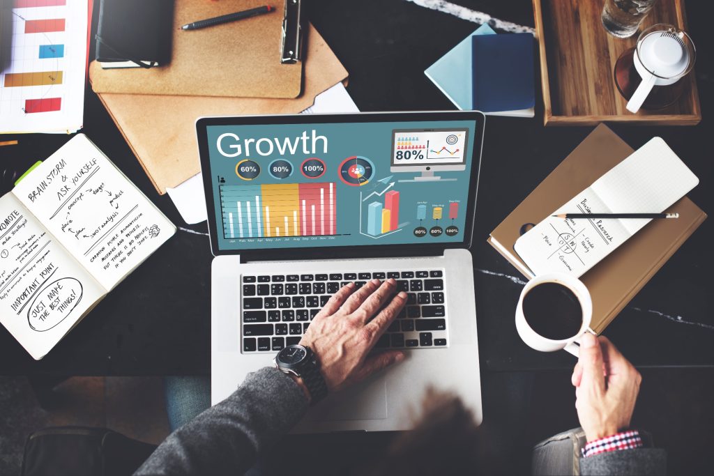 Professional analyzing growth metrics and business valuation on laptop at desk with coffee and planning documents