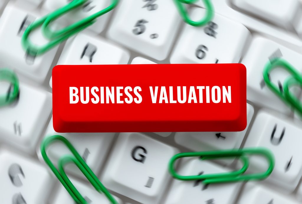 Red button labeled "BUSINESS VALUATION" on keyboard with green paper clips