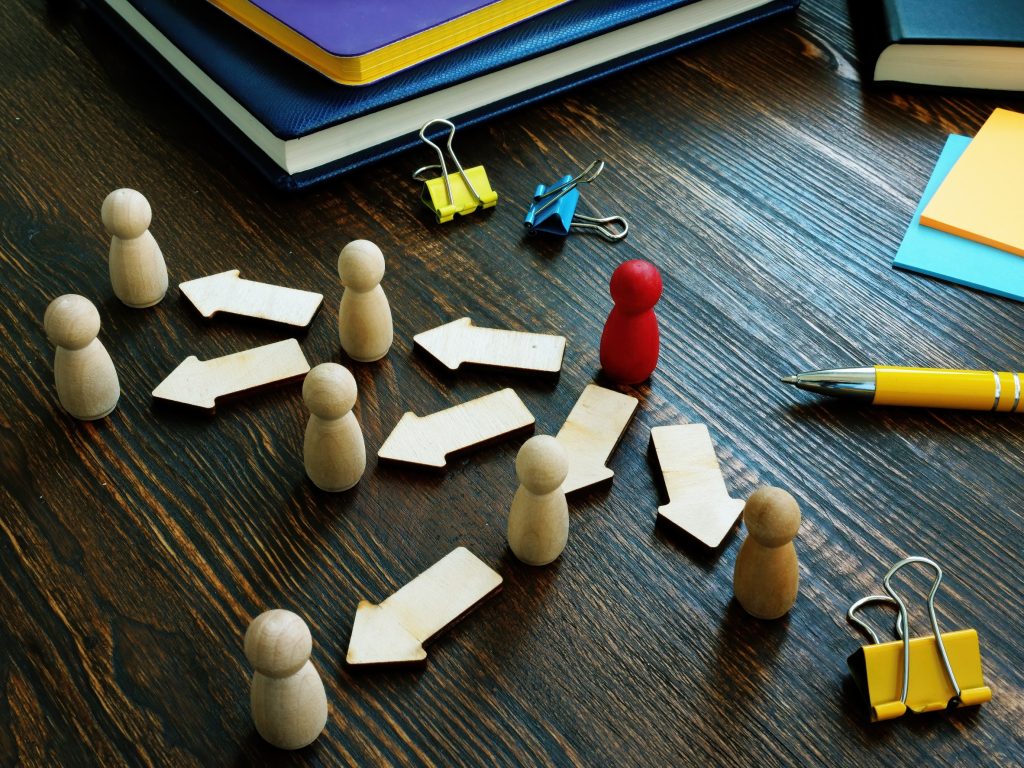 Red wooden peg standing out from group of tan pegs, symbolizing leadership and individual responsibility among a team