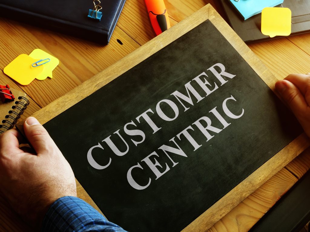 Person holding tablet displaying "Customer Centric" text on wooden desk workspace