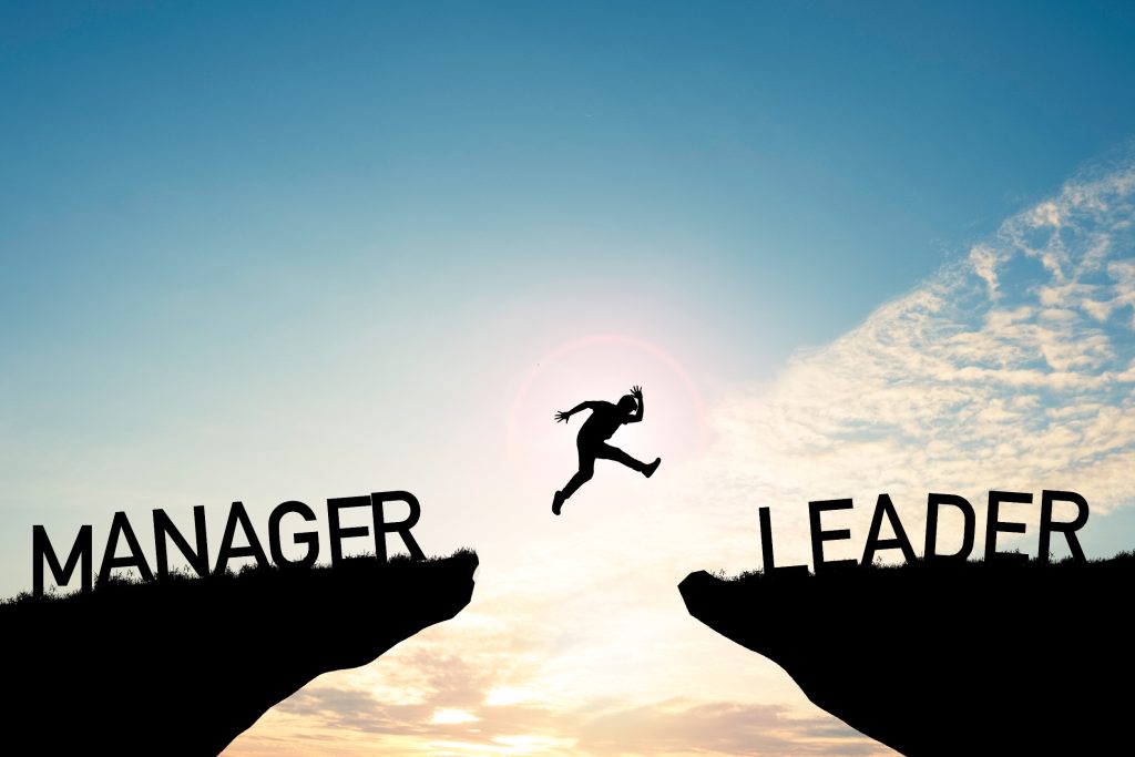 Silhouette of professional leaping between two cliffs labeled "Manager" and "Leader