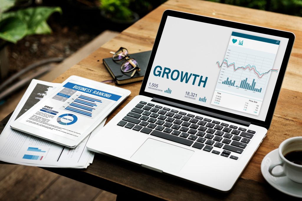 Laptop displaying growth analytics dashboard with financial charts and documents on wooden desk