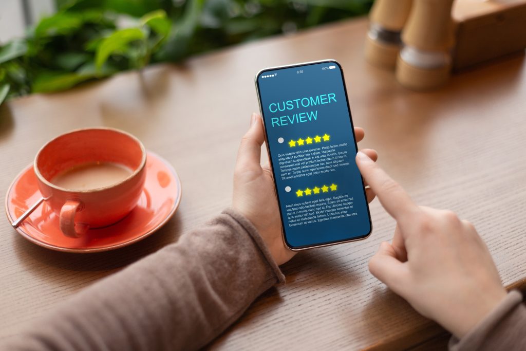 Person holding smartphone displaying customer feedback interface, with coffee cup on desk