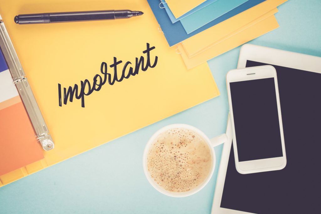 Workspace with "Important" note, coffee cup, smartphone, and notebook illustrating business priorities and focus