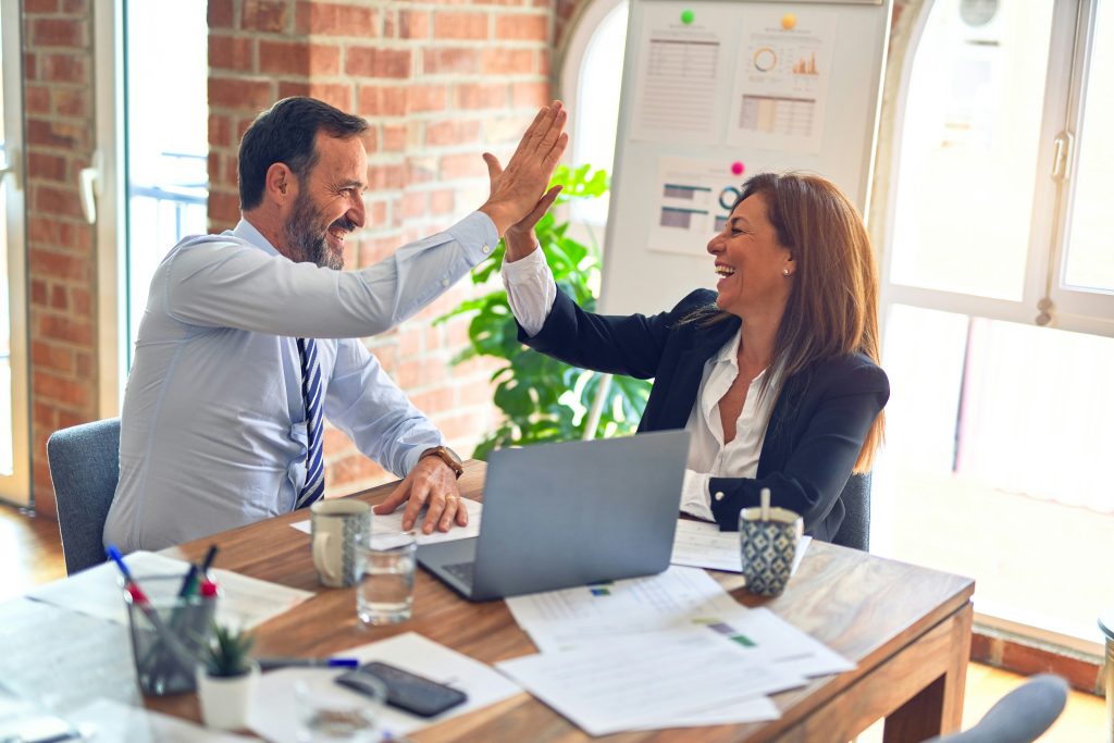 Two professionals high-fiving at desk while discussing customer insights and business growth