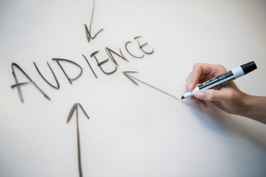 Hand writing "AUDIENCE" with arrows pointing inward, illustrating focus on customer base strategy