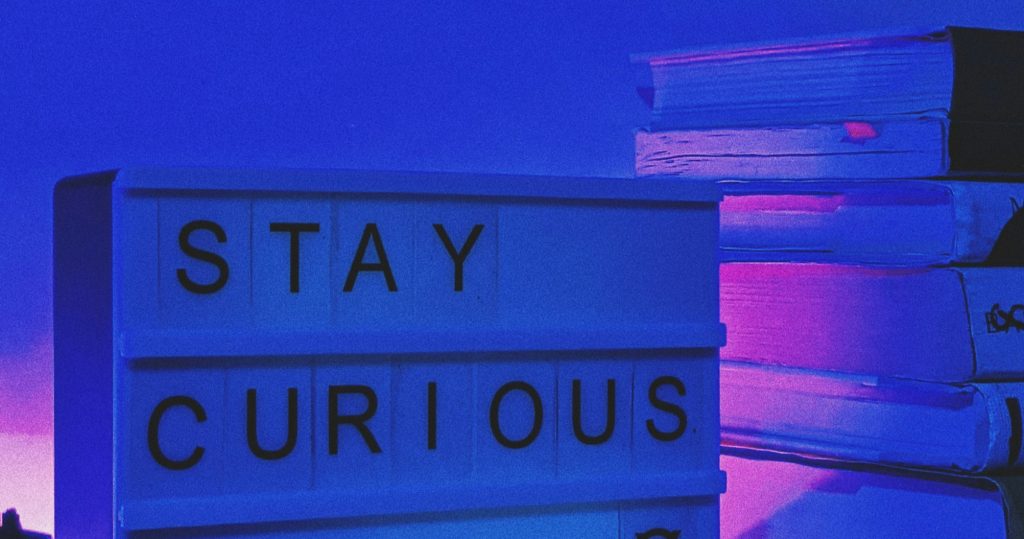 Neon signs reading "STAY CURIOUS" against twilight sky, symbolizing curiosity as essential leadership trait