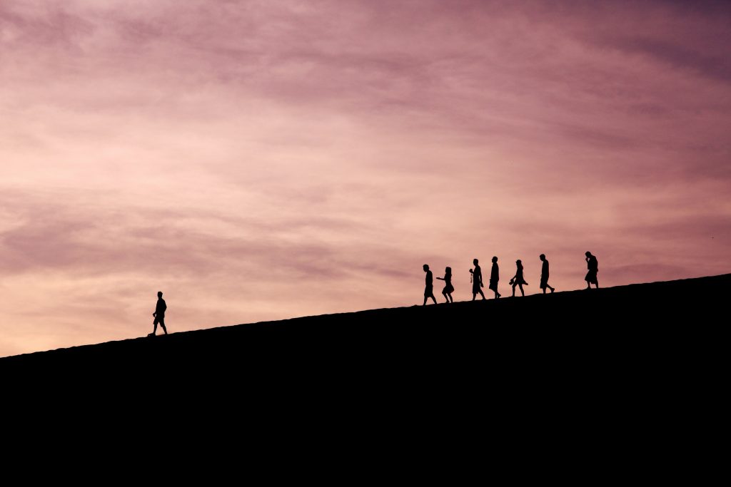 Silhouettes of team members standing together on a hilltop against a purple sunset sky