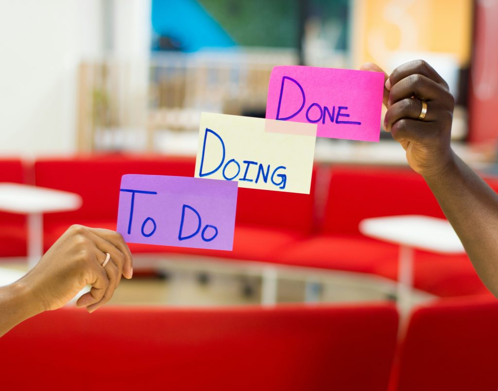 Hands holding sticky notes labeled "To Do," "Doing," and "Done" to illustrate task prioritization and workflow management