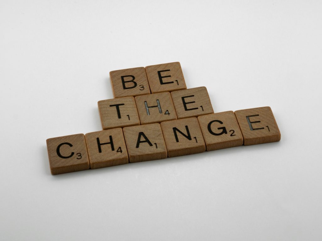 Wooden Scrabble tiles spelling "BE THE CHANGE" arranged on white surface
