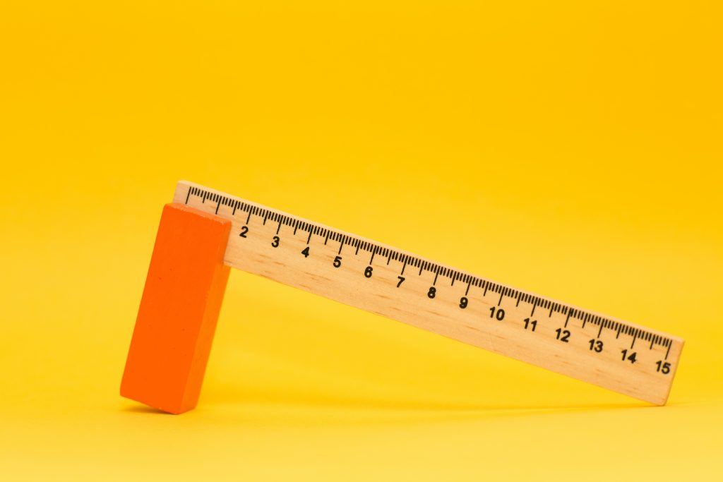 Measuring activity versus managing outcomes: ruler and orange block on yellow background