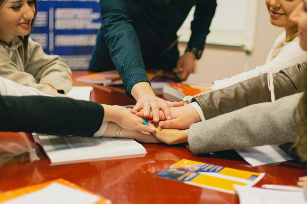 Team members stacking hands in unity gesture over table with work materials