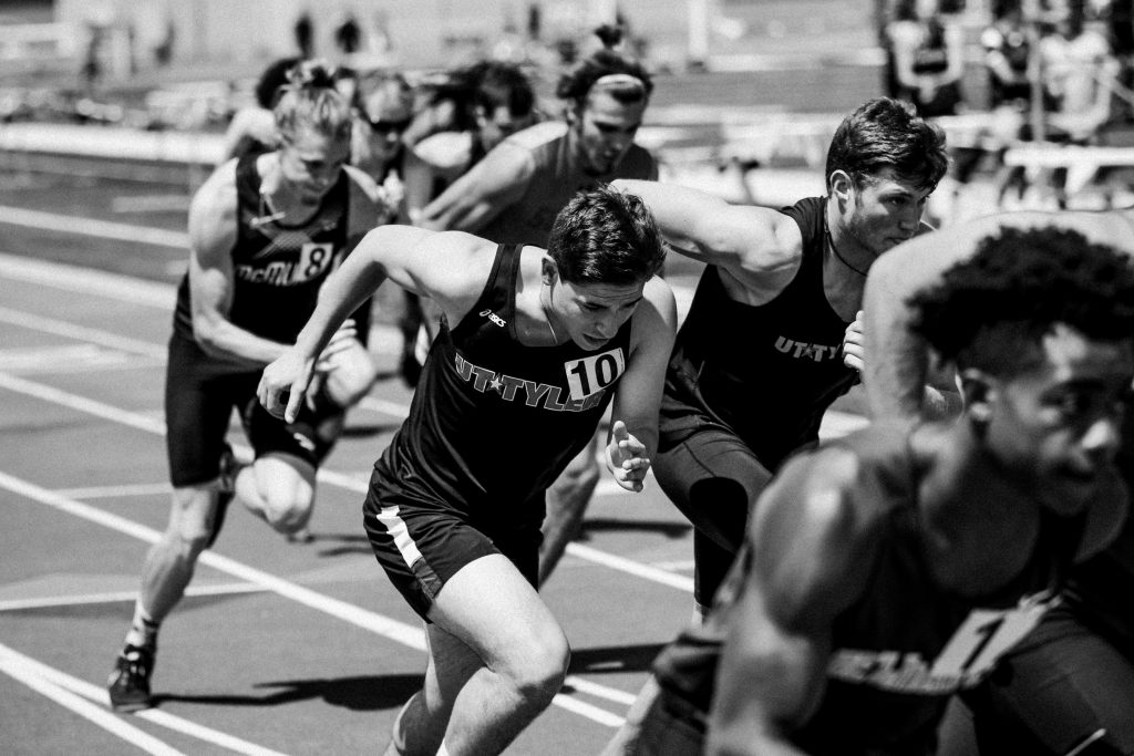 Black and white photo of athletes in relay race executing baton handoff, symbolizing seamless team coordination and adaptive