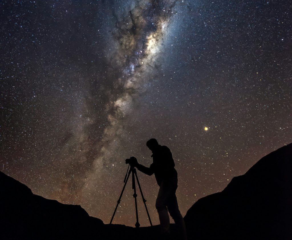 Silhouetted astronomer with telescope observing Milky Way galaxy at night