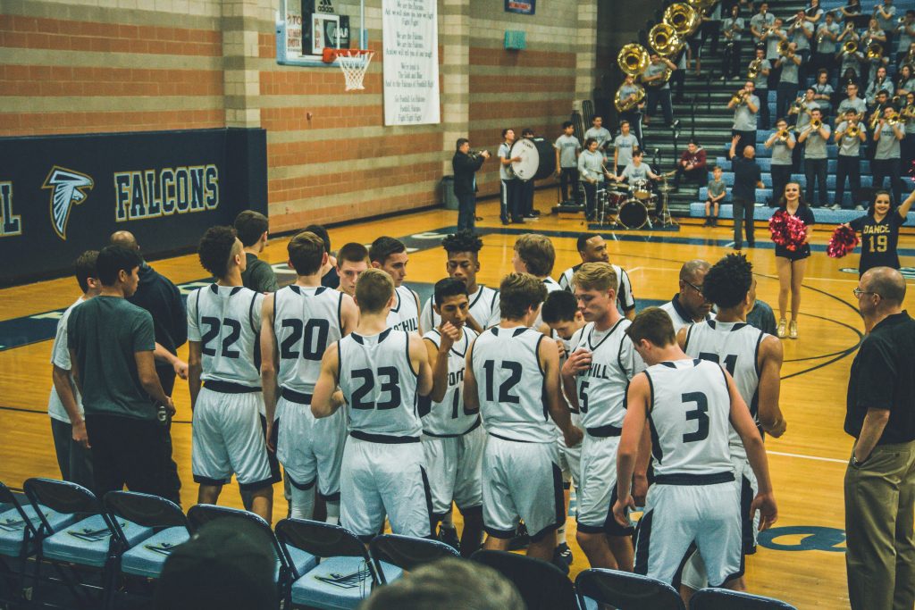 Basketball team huddled together in gym during timeout, demonstrating team unity and shared commitment
