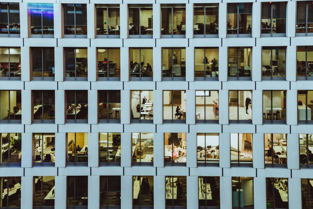 Aerial view of apartment building facade with regularly spaced windows showing varied interior lighting and furnishings
