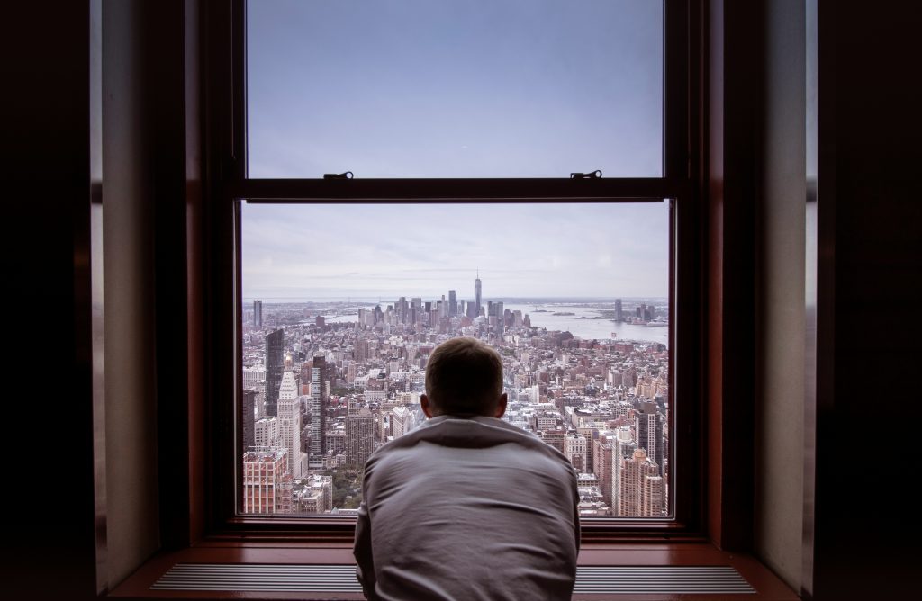 Person viewing cityscape from high-rise window, symbolizing leadership perspective and strategic vision