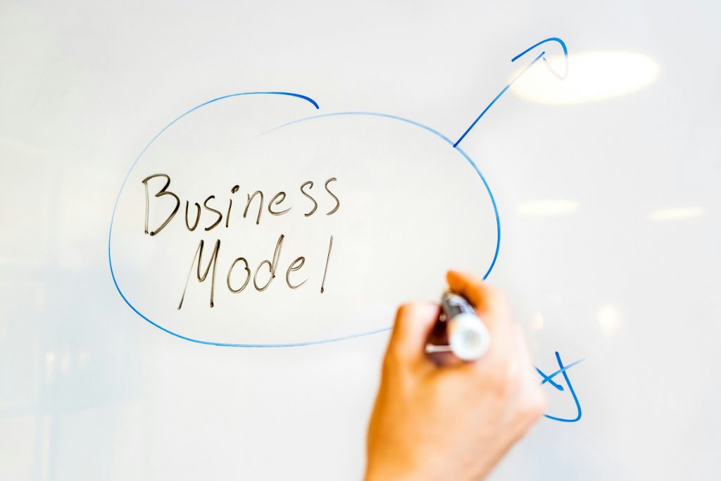 Hand drawing "Business Model" label on whiteboard with blue marker and arrows