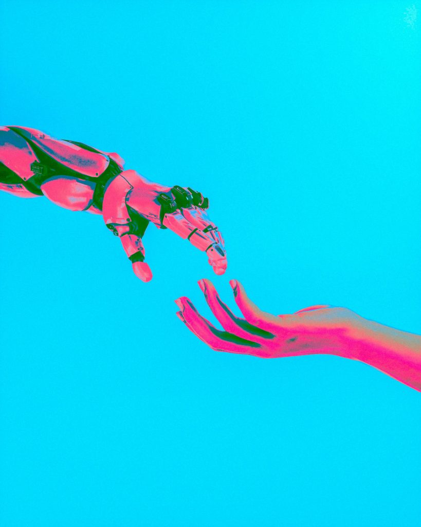 Neon pink robot hand reaching toward human hand on cyan background, symbolizing AI as a tool supporting human strategy