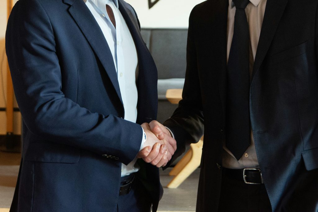 Two businessmen in formal attire shaking hands in professional setting