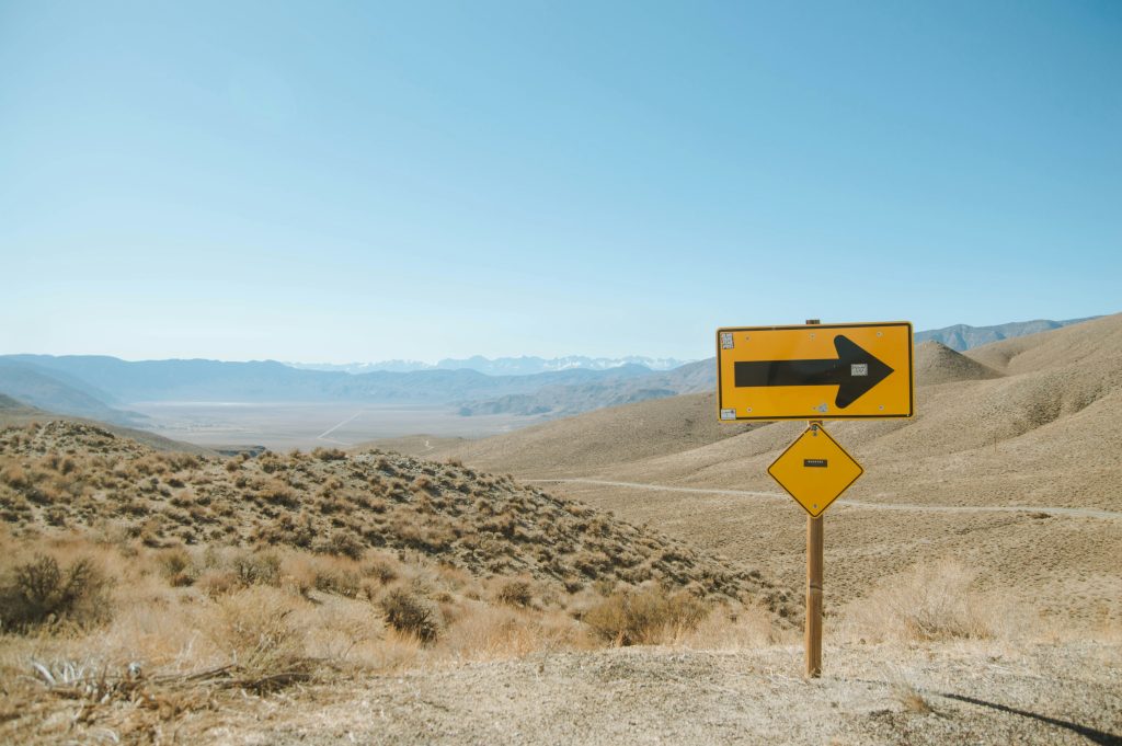 Yellow directional arrow sign on desert road pointing toward mountains, symbolizing clear path forward through uncertainty