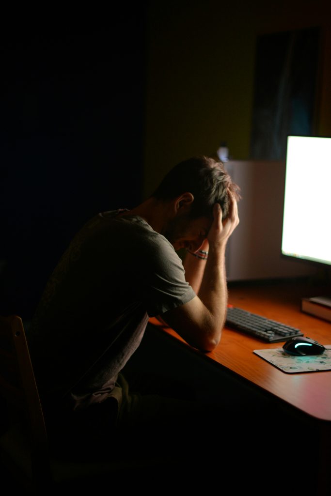 Person experiencing burnout at desk under bright screen light, illustrating executive stress and fatigue