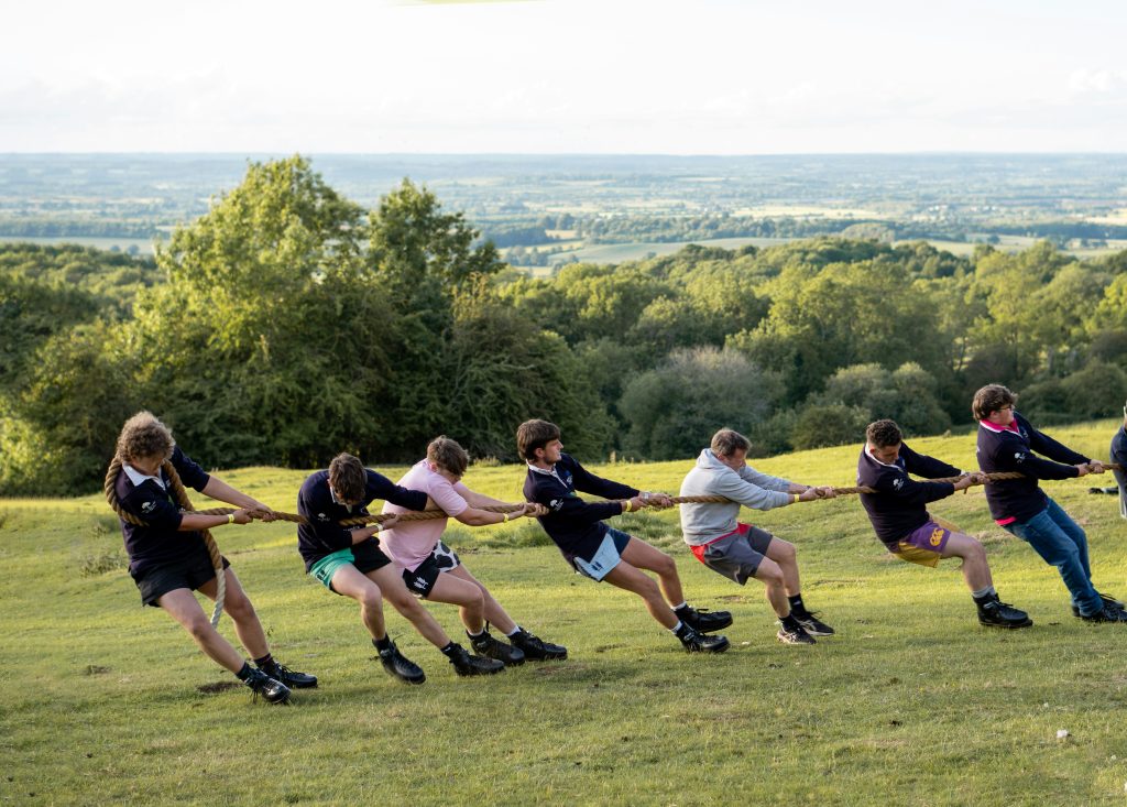 Team of youth pulling together in a tug-of-war game on a hillside field