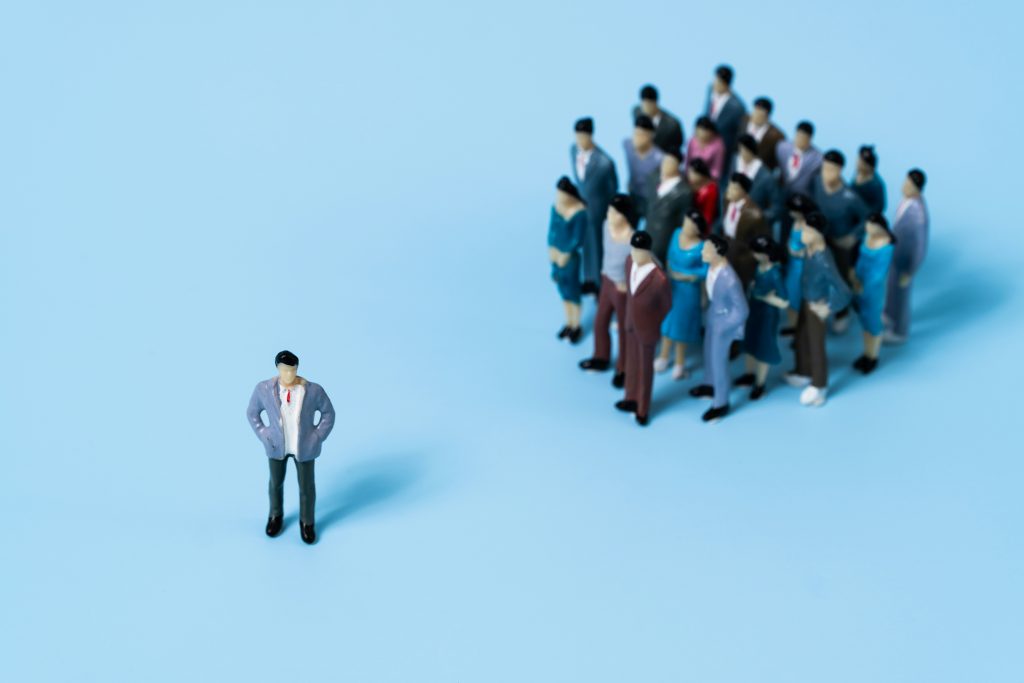 One person standing apart from a large group on blue background, illustrating business differentiation concept